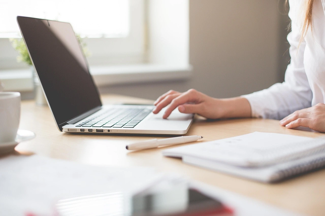 A professional copywriter or digital marketer typing on a laptop at a bright, clean desk with a notebook and coffee, representing blog and content creation.