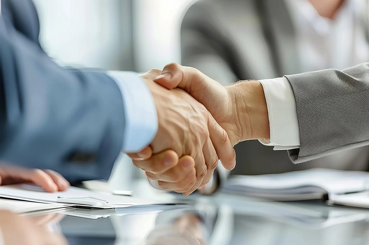 Close-up of a professional handshake between two people in business attire, symbolizing a successful partnership and client agreement.